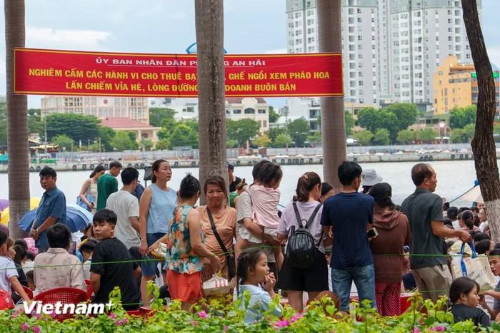Người dân trật tự ngồi xem pháo hoa phía sau hàng rào và băng rôn cấm lấn chiếm vỉa hè kinh doanh. (Ảnh: Thanh Phong/Vietnam+)
