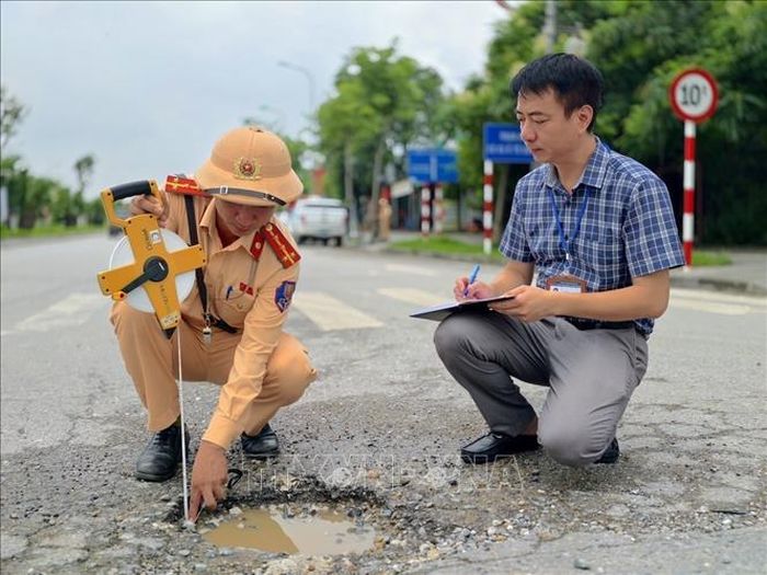Cán bộ Đội Cảnh sát giao thông đường bộ số 15 (Phòng Cảnh sát giao thông Hà Nội) kiểm tra hiện trạng mặt đường Lê Hữu Tựu, ghi nhận các vị trí bong tróc, hư hỏng mặt đường trong quá trình khảo sát thực tế. Ảnh: Trung Nguyên/TTXVN