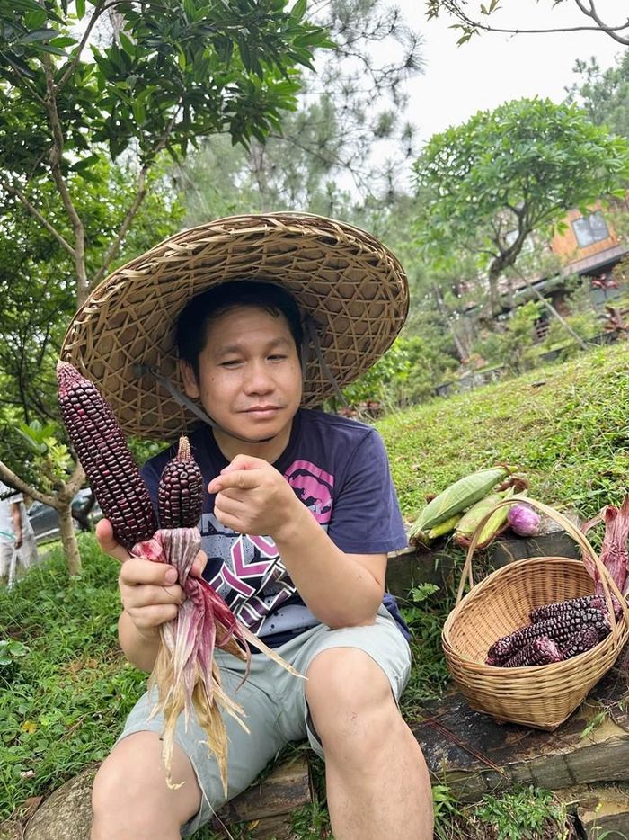 Trọng Tấn cầm 2 bắp ngô tím ngắm nghía như đang so sánh độ mẩy hạt. Nụ cười mãn nguyện cho thấy niềm vui giản dị của một "nông dân" tay ngang.