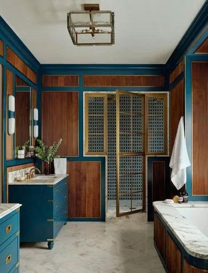 Phòng tắm được cải tạo hoàn toàn với bồn tắm ngâm, khu tắm đứng riêng và hai bàn trang điểm đặt làm theo yêu cầu. Gỗ óc chó có vân sọc kết hợp cùng đá cẩm thạch và các chi tiết đồng đánh bóng mang lại cảm giác ấm áp, mềm mại cho không gian vốn sử dụng nhiều vật liệu cứng. Hai tủ lavabo màu xanh ngọc tạo điểm nhấn nhẹ nhàng nhưng đủ khác biệt trong tổng thể.