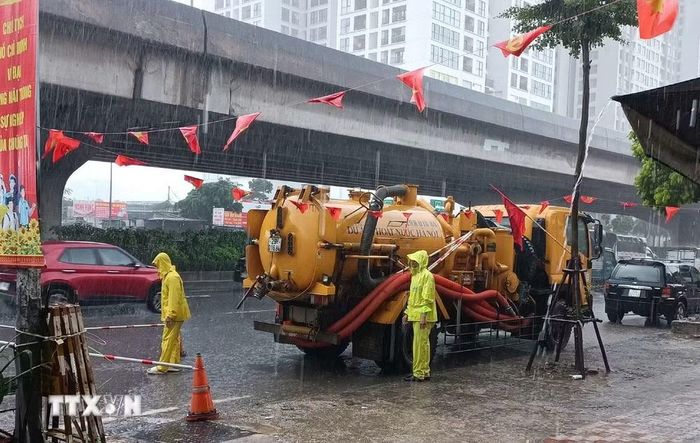 Công nhân ứng trực tiêu thoát nước trong mưa lớn tại đường Nguyễn Xiển. (Ảnh: Nguyễn Thắng/TTXVN)