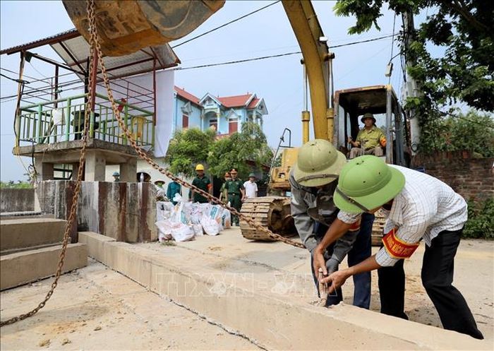 Ngày 15/7/2026, lực lượng xung kích kiểm tra móc xích của phương tiện cơ giới trước khi nâng tấm phai tại cửa khẩu đê Đô Tân. Ảnh: Trung Nguyên/TTXVN
