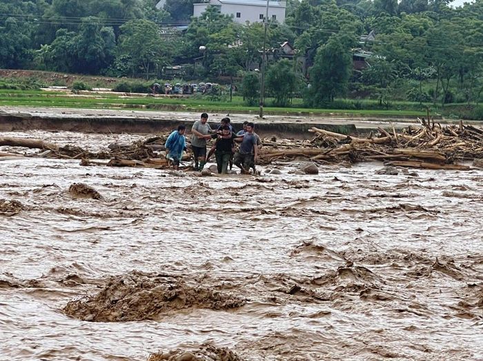 Cán bộ công an cùng người dân nắm chặt tay nhau, tạo thành "sợi dây người" vượt dòng lũ xiết để cứu nạn. Ảnh: A Chài.