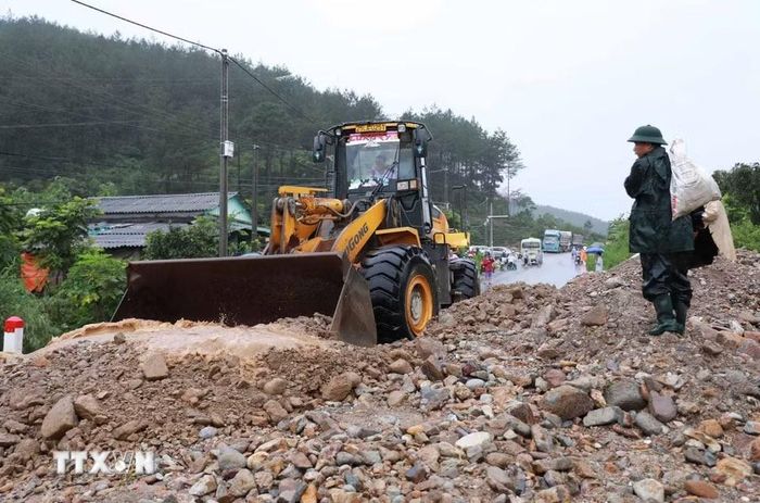 Lực lượng chức năng huy động phương tiện máy móc khắc phục hót sạt sụt trên Quốc lộ 32 sau khi cơn lũ đi qua. (Ảnh: Quý Trung/TTXVN)