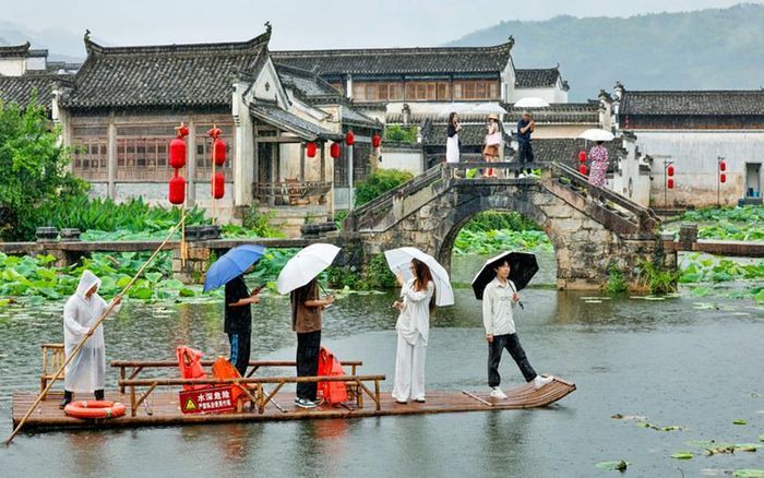 Khách du lịch trải nghiệm tour đi bè gỗ trên sông ngày 29/6, ngắm vẻ đẹp trong mưa của một làng cổ tại Hoàng Sơn (địa cấp thị thuộc tỉnh An Huy - nơi nổi tiếng với nhiều di sản thế giới như dãy núi Hoàng Sơn và các làng cổ). Ảnh: VCG