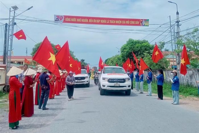 Người dân cầm cờ Tổ Quốc đứng dài hai bên đường đón hài cốt liệt sĩ Hoàng Minh Chính trở về.