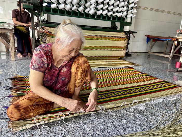 Bà Nguyễn Thị Liên Hoa tay vẫn thoăn thoắt chỉnh viền và cắt tỉa những sợi chỉ thừa trên chiếc chiếu cờ.