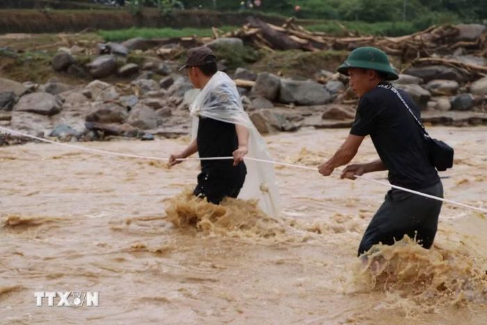 Nước lũ nhiều chỗ vẫn chảy xiết, lực lượng cứu hộ phải căng dây để hỗ trợ người dân di chuyển an toàn. (Ảnh: Nguyễn Oanh/TTXVN)