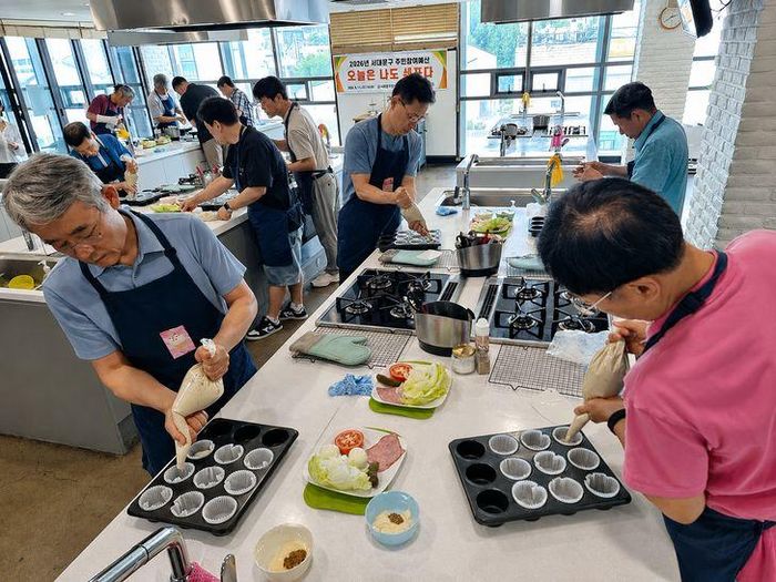 Các học viên cho bột bánh muffin việt quất vào khuôn trong lớp học "Tự lập trong căn bếp dành cho nam giới trung niên – Hôm nay tôi là đầu bếp" tại bếp cộng đồng ở quận Seodaemun, Seoul (Hàn Quốc). Ảnh: Korea Times