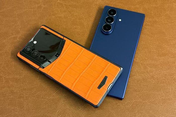 Vertu Alphafold bọc da màu cam đặt cạnh một mẫu điện thoại gập Samsung. Ảnh: TechCrunch.
