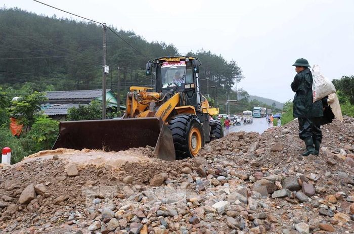 Lực lượng chức năng huy động phương tiện máy móc khắc phục hót sạt sụt trên Quốc lộ 32 sau khi cơn lũ đi qua. Ảnh: Quý Trung - TTXVN