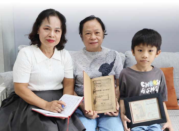 Tác giả (bìa trái) cùng chị Lê Kim Hương (ngồi giữa) bên hồ sơ kỷ vật của mẹ - y sĩ Nguyễn Kim Mến. Ảnh: TRẦM HƯƠNG