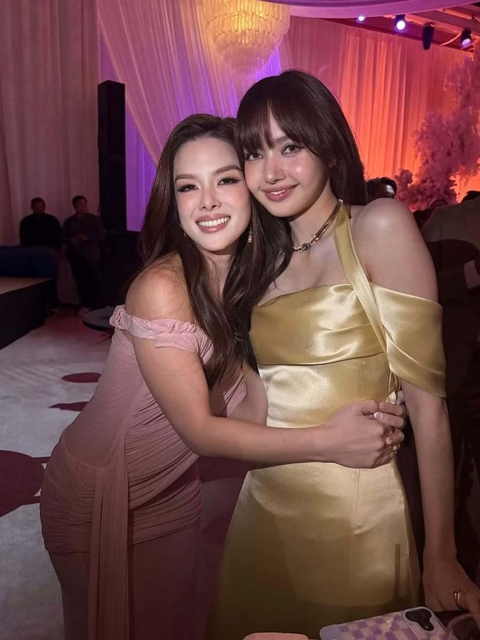 Lydia Sarunrat ôm Lisa khi gặp nhau tại tiệc cưới. Hai nghệ sĩ thu hút sự chú ý với phong cách đối lập. Lydia nữ tính trong đầm trễ vai màu hồng, còn thành viên BlackPink nổi bật với thiết kế lụa vàng ánh kim.