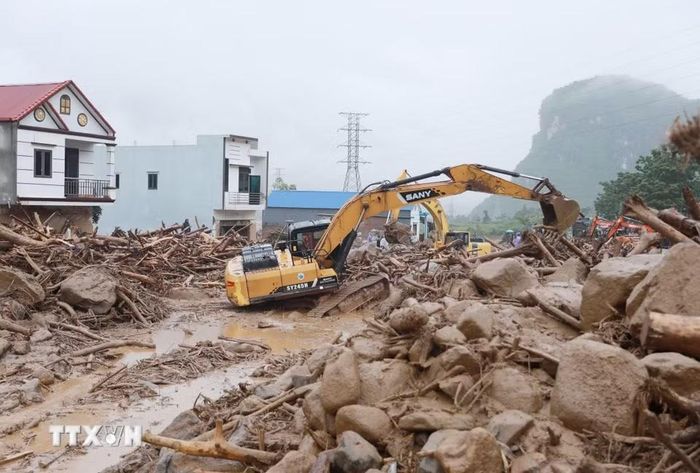 Các phương tiện máy móc tập trung san gạt cây cối, đất đá góp phần thông đường tạm thời cho nhân dân đi lại. (Ảnh: Quý Trung/TTXVN)