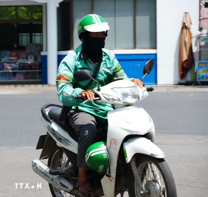 Lái xe công nghệ mặc đồ bảo hộ chống nắng nóng gay gắt khi di chuyển trên đường Trần Hưng Đạo, phường Phú Xuân, thành phố Huế. (Ảnh: Nguyên Lý/TTXVN)
