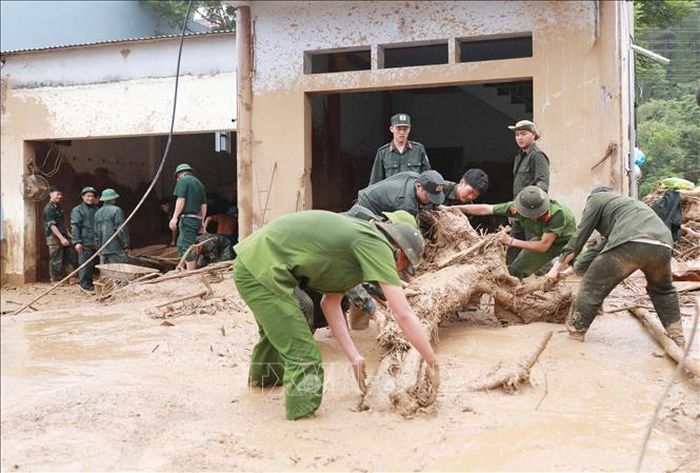 Lực lượng Công an giúp dân dọn bùn đất, đá, cây gỗ trôi vào nhà tại xã Mường Than. Ảnh: Quý Trung/TTXVN