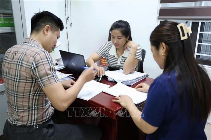 Cán bộ địa phương hỗ trợ người dân thực hiện các thủ tục để đóng mã số thuế. Ảnh: Hoàng Ngà/TTXVN