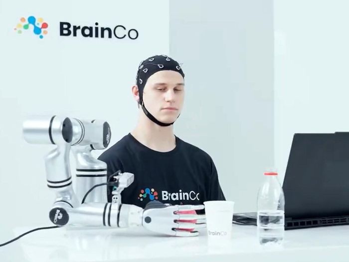 Một người dùng công nghệ điều khiển bằng ý nghĩ của BrainCo đang điều khiển robot lấy một quả táo.