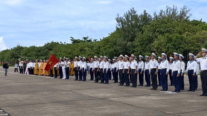 Các đại biểu trong Đoàn công tác cùng cán bộ, chiến sĩ và nhân dân trên đảo đứng nghiêm, hướng về quốc kỳ