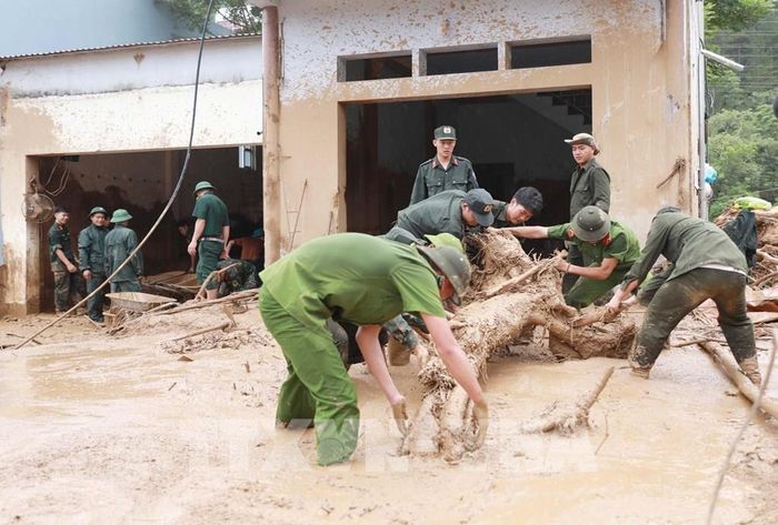 Lực lượng Công an giúp dân dọn bùn đất, đá, cây gỗ trôi vào nhà tại xã Mường Than. Ảnh: Quý Trung - TTXVN