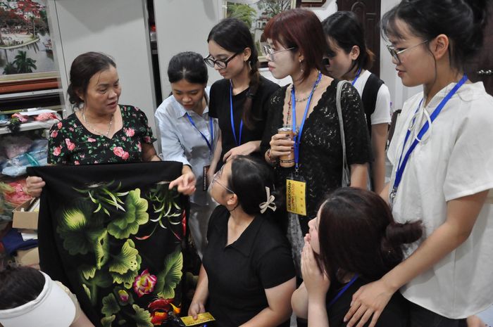 Nghệ nhân Hoàng Thị Khương giới thiệu cho các bạn trẻ về các sản phẩm của làng nghề thêu Quất Động (Hà Nội). Ảnh: BTC