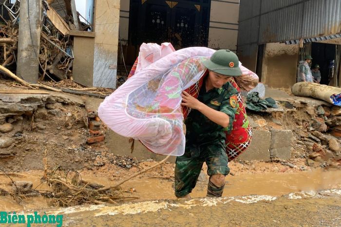 Cán bộ Bộ đội Biên phòng đội mưa, đưa chăn màn và đồ dùng thiết yếu của người dân ra khỏi khu vực bị lũ quét tàn phá. Ảnh: Văn Hợi