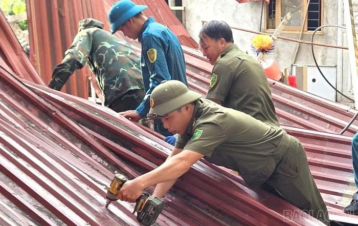 Các lực lượng phối hợp hỗ trợ hộ dân thôn Lâm Tiến khắc phục phần mái nhà bị tốc mái.