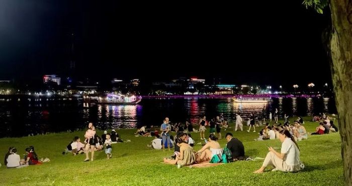 Người dân và các bạn trẻ thư giãn, picnic trên bãi cỏ ven sông Hương vào buổi tối.