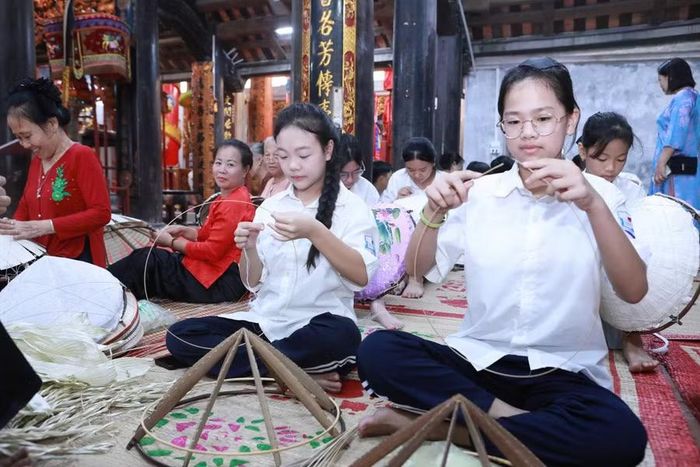 Các em học sinh được các nghệ nhân truyền nghề làm nón lá làng Chuông. Ảnh: Đình Tuệ.