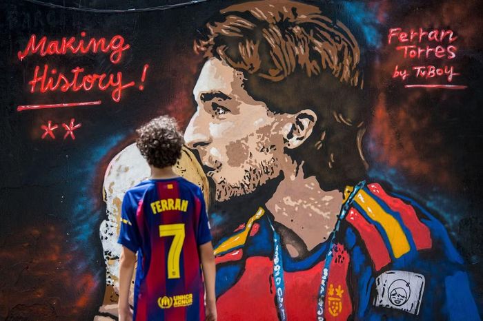 Ferran Torres trở thành người hùng của Tây Ban Nha sau cú ghi bàn giúp đội bóng vô địch World Cup 2026. Bức tranh “Making History!” (tạm dịch: Tạo nên lịch sử) xuất hiện tại Barcelona sau khi Ferran Torres ghi bàn quyết định ở trận đối đầu Argentina. Hình ảnh cậu bé mặc áo số 7 đứng trước chân dung Ferran gợi lại hành trình từ giấc mơ thời thơ ấu đến vị thế người hùng bóng đá Tây Ban Nha.