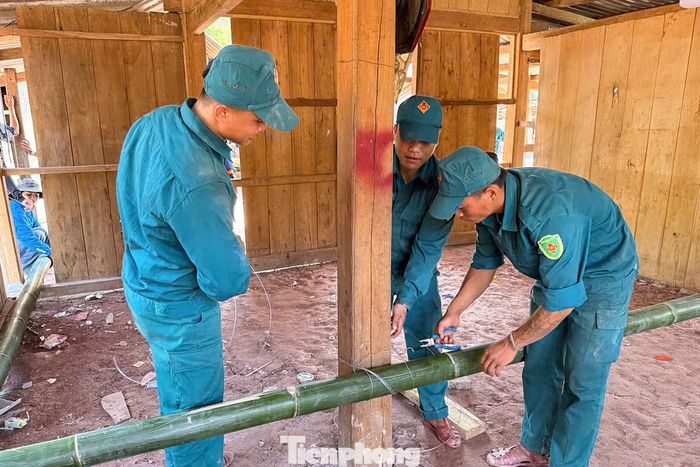 Bàn ghế, tủ gỗ, bao lúa, vật dụng sinh hoạt… lần lượt được đưa ra ngoài. Sau đó, các tình nguyện viên dùng những cây tre lớn chằng dọc theo khung nhà, gia cố chắc chắn rồi cùng nhau giữ chặt thanh tre, dồn sức nâng, kéo. Theo từng nhịp hô, hàng chục “thần đèn áo xanh” kéo căn nhà gỗ nặng từ từ nhích khỏi vị trí cũ, tiến về khu đất mới cách đó vài chục mét.