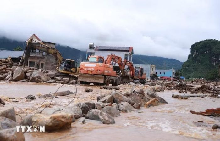 Các phương tiện máy móc tập trung san gạt cây cối, đất đá góp phần thông đường tạm thời cho nhân dân đi lại. (Ảnh: Quý Trung/TTXVN)