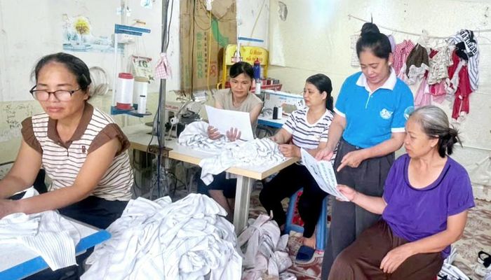 Bà Phạm Thị Vẻ - Chủ tịch Hội LHPN xã Lương Tài tuyên truyền và phát tờ rơi về tiết kiệm điện mùa hè tại xưởng may của chị Trần Thị Luyến- chi hội phụ nữ thôn Phượng Sơn