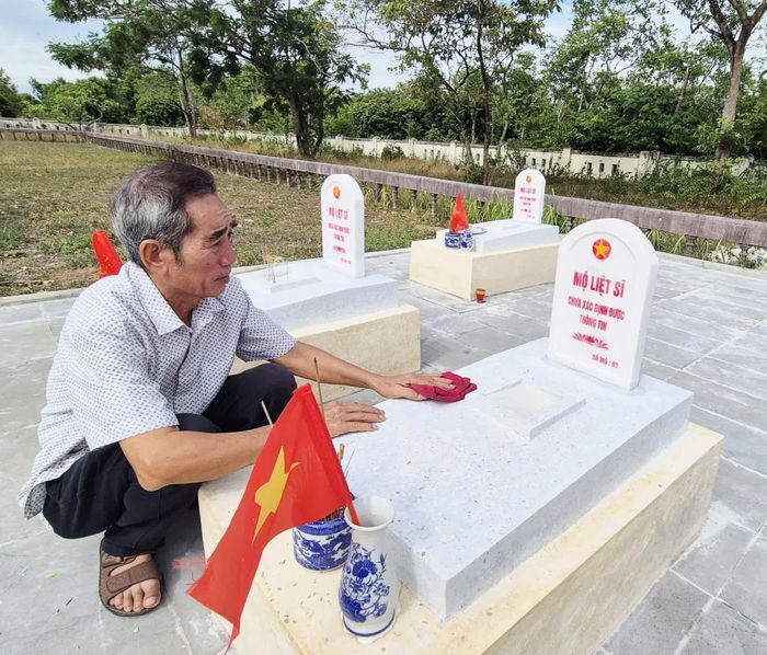 Ông Nguyễn Ngọc Tân cẩn mẫn lau chùi, chăm sóc chu đáo từng phần mộ liệt sĩ như người thân ruột thịt của mình - Ảnh: K.S