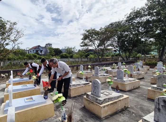 Ông Nguyễn Ngọc Tân (bên phải ngoài cùng) và anh Hồ Văn Phương (bên trái ngoài cùng) thắp hương tại các phần mộ liệt sĩ vừa được quy tập về nghĩa trang - Ảnh: K.S