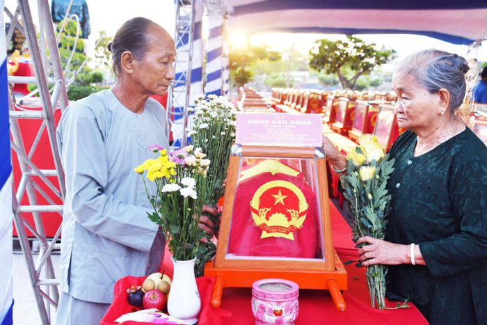 Bà Đặng Thị Bé (chị ruột) và ông Đặng Văn Hùng (em ruột) liệt sĩ Đặng Văn Dùng (Dũng) bên hài cốt liệt sĩ em trai mình do Đội K93 tìm kiếm, quy tập. Ảnh: Trung Thắng