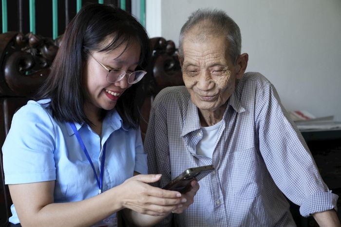 Cán bộ Hoàng Thị Dưỡng hỗ trợ cụ ông Nguyễn Xuân Tùng thực hiện thủ tục "Cấp bổ sung hoặc cấp lại Giấy chứng nhận người có công" tại nhà riêng. Ảnh: NT