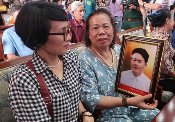 Bà Nguyễn Thị Thuận cùng bức ảnh chân dung liệt sĩ Hoàng Văn Khế được phục dựng. (Ảnh: Phạm Thương)
