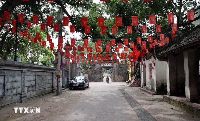 Không gian bên trong làng Ước Lễ với tuyến đường gạch cổ dẫn ra cổng làng, rợp cờ Tổ quốc và cờ Đảng, lưu giữ đậm nét kiến trúc truyền thống của một làng cổ vùng đồng bằng Bắc Bộ. (Ảnh: Vũ Quang/TTXVN)