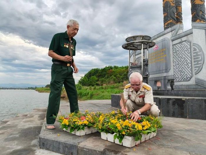 Ông Lê Bá Dương chuẩn bị hoa thả xuống sông, sau lưng là bia đá khắc thơ ông.