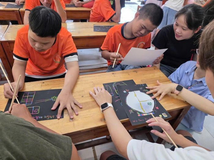 Các tình nguyện viên nhóm từ thiện Cộng đồng Nakưnê hướng dẫn các em trải nghiệm học kỹ năng vẽ tranh cào. Ảnh do trung tâm cung cấp
