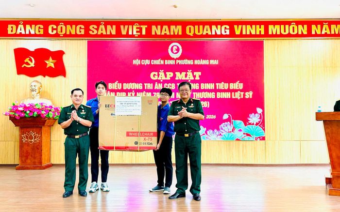 Chủ tịch Hội Cựu chiến binh phường Hoàng Mai Nguyễn Văn Xuân (bên phải) tiếp nhận chiếc xe lăn từ đại diện doanh nghiệp để trao tặng thương binh Hoàng Ngọc Thành. Ảnh: Trần Oanh.