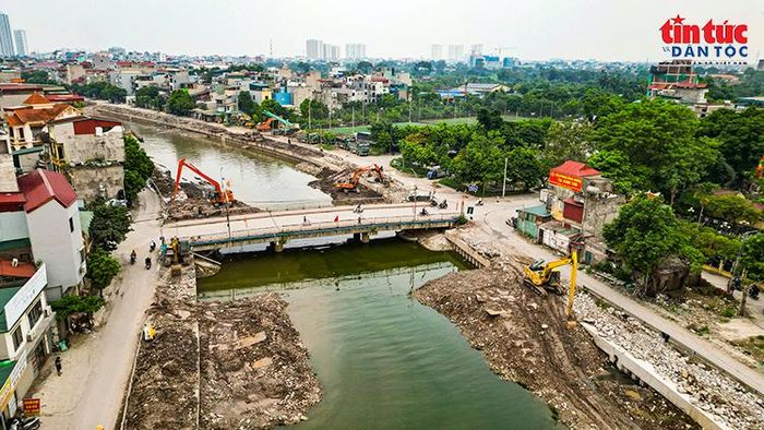Toàn cảnh khu vực thi công quanh cầu, với nhiều máy xúc hoạt động ở hai bên bờ sông.