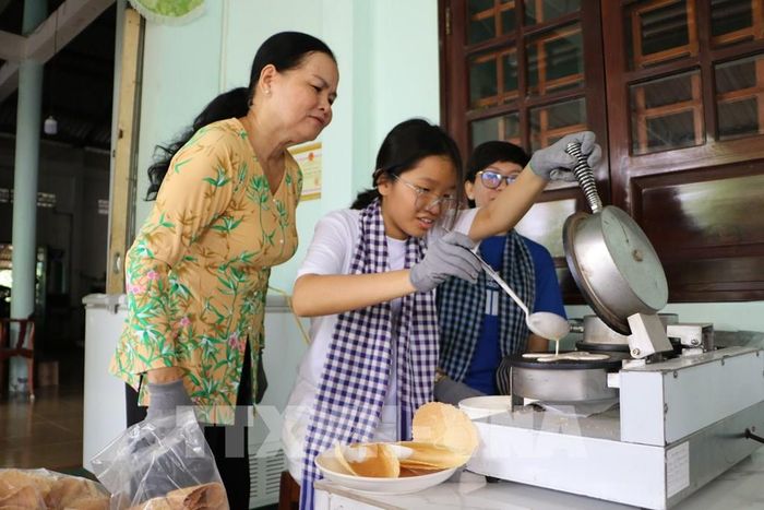 Du khách trải nghiệm làm bánh kẹp xoài tại Di tích Phủ thờ Thư Ngọc Hầu (xã Mỹ Thọ). Ảnh: Hồng Thái - TTXVN