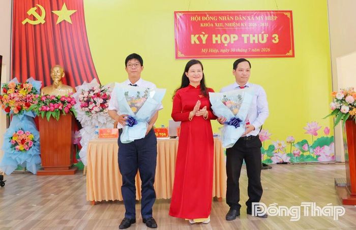 Đồng chí Trần Thị Bích Du, Bí thư Đảng ủy, Chủ tịch HĐND xã Mỹ Hiệp tặng hoa chúc mừng đồng chí Huỳnh Công Hiển (bìa trái) được tín nhiệm bầu giữ chức Phó Chủ tịch UBND xã và đồng chí Lê Văn Bình (bìa phải) được tín nhiệm bầu giữ chức Ủy viên UBND xã, nhiệm kỳ 2026 - 2031.
