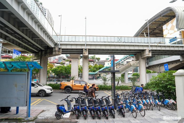 Trạm xe đạp và xe máy điện công cộng nằm gọn gàng ngay dưới chân nhà ga đường sắt trên cao. Việc bố trí điểm đỗ xe đạp, xe máy điện công cộng tại bến xe, ga Metro, trường học và xây dựng làn đường riêng cho xe đạp giúp hoàn thiện mảnh ghép "chặng đầu - chặng cuối" trong chuỗi giao thông xanh. (Ảnh: Bãi cho thuê xe đạp và xe điện dưới ga Láng).