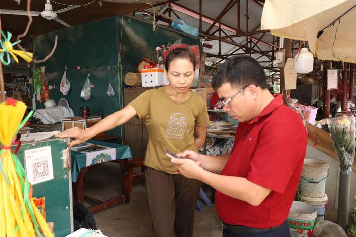 Cán bộ Agribank hỗ trợ tiểu thương ở chợ Thượng Lâm (xã Phúc Sơn) cài đặt ứng dụng Agribank Plus. Ảnh: Kim Nhuệ
