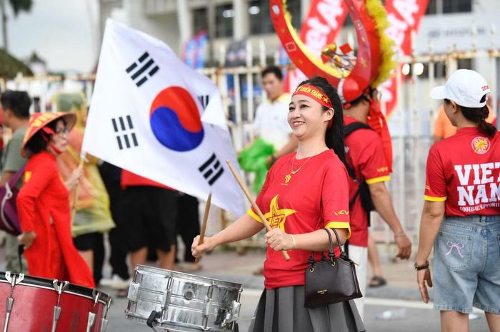 Xung quanh sân, sắc đỏ ngày càng phủ kín khi thời điểm khai cuộc đến gần. Những tiếng hô "Việt Nam! Việt Nam!", tiếng trống và những lá cờ tung bay trong mưa tạo nên bầu không khí cuồng nhiệt, hứa hẹn biến Mỹ Đình thành điểm tựa tinh thần lớn cho đội chủ nhà.