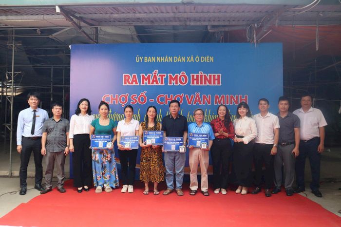 Lãnh đạo xã Ô Diên và các ngân hàng tặng tiểu thương mã quyét QR thực hiện thanh toán không dùng tiền mặt. Ảnh: NM