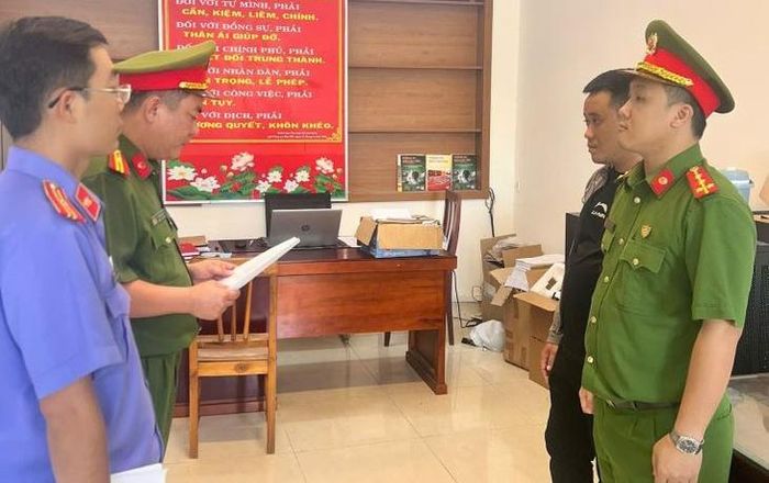 Cơ quan CSĐT Công an tỉnh Khánh Hòa tống đạt quyết định khởi tố bị can Nguyễn Quang Vinh (áo đen). Ảnh: CAKH